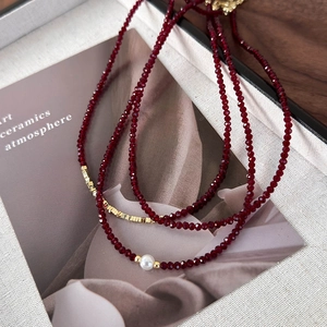 Close-up of deep red beaded necklace with a white pearl and gold accents on soft fabric