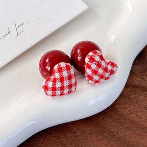 Detailed view of red bead and checkered cloth heart earrings on white ceramic dish