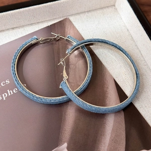 Detail view of large silver hoop earrings wrapped in light blue denim fabric with silver dots