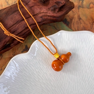 Gros plan du pendentif gourde en bois poli sur une corde tressée orange et perle dorée