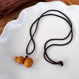 Vue détaillée du pendentif gourde en bois sur corde tressée marron foncé