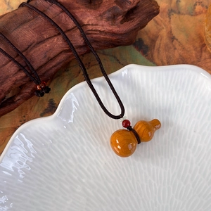 Vue détaillée du pendentif gourde en bois sur plateau en céramique avec cordon tressé à la main