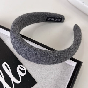 Close-up of a grey knitted headband with a black 'HAND MADE' label and soft texture