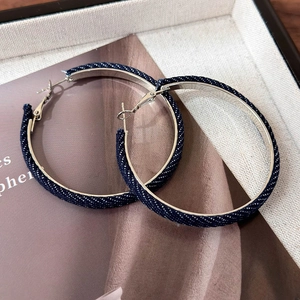 Close-up of silver metal hoop earrings wrapped in dark blue denim fabric texture