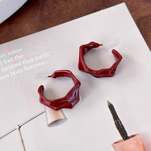 Detailed view of deep red irregular C-shape earrings with textured enamel finish on paper