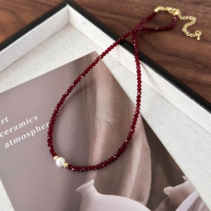 Detailed macro of a deep red beaded necklace with a white pearl and gold lobster clasp