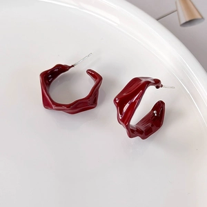 Detailed side view of irregular pleated burgundy enamel hoop earrings on ceramic tray