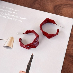 Macro detail of deep red pleated hoop earrings with glossy irregular wave texture