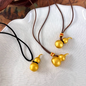 Traditional gold gourd pendant necklaces with matte finish and woven cord on a ceramic plate