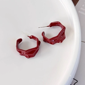 Macro detail of burgundy textured C-shape hoop earrings with molten lava pattern