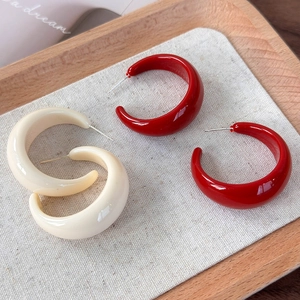 Détail de boucles d'oreilles créoles en résine en forme de C en rouge brillant et blanc