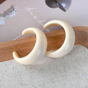 Gros plan de boucles d'oreilles créoles en résine blanc crème sur plateau en bois