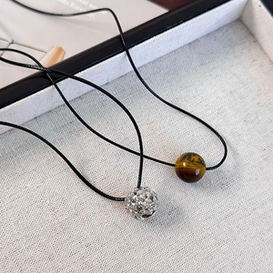 Détail d'une sphère argentée texturée et de pendentifs oeil de tigre sur cordons noirs