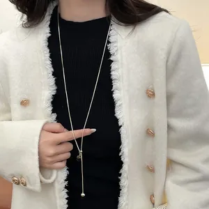 Detail of adjustable gold Y-necklace featuring polished metal sphere pendants on a model