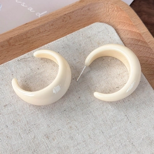 Gros plan détaillé de boucles d'oreilles créoles en résine crème sur plateau en bois
