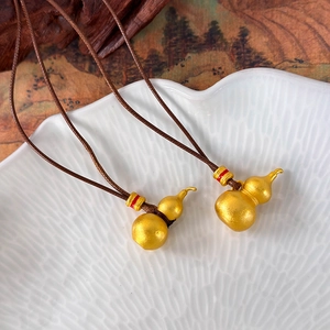 Detail of golden frosted gourd pendant on brown woven cord over white ceramic plate