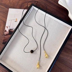 Détail du collier en corde noire avec perle marron foncé et pendentifs goutte dorés