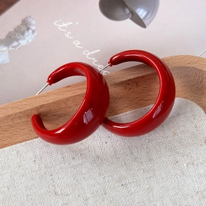 Gros plan de boucles d'oreilles créoles C rouges vintage sur un plateau en bois
