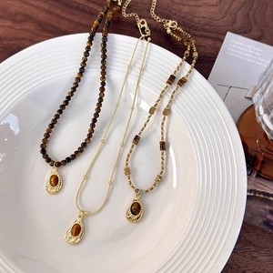 Three tiger eye stone necklaces with gold teardrop pendants on a white porcelain plate