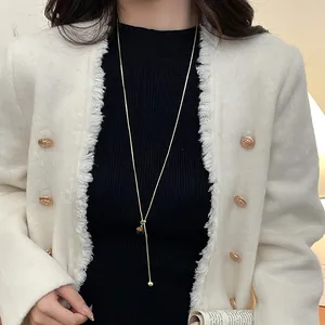 Detailed view of a long gold sweater necklace with tiger eye beads on a model