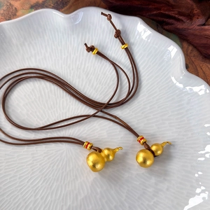 Detailed macro view of two matte gold gourd pendants on adjustable brown braided cords