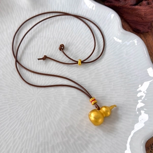 Detail view of gold gourd pendant with matte finish and red lacquer accent ring