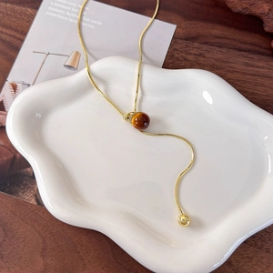 Elegant gold snake chain necklace with round tiger eye bead on a white ceramic tray