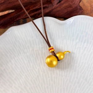 Detailed close-up of a gold gourd pendant on a brown braided cord with red accents