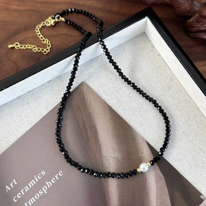 Detail view of black faceted bead necklace with a white pearl on elegant linen display