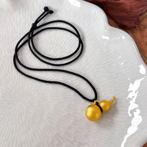 Macro shot of matte gold gourd pendant with a black woven cord on white ceramic