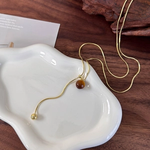 Detail of tiger eye stone pendant on golden snake chain over a ceramic plate