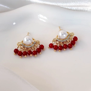 Elegant gold fan earrings with white pearls, rhinestones and red bead tassels on a tray
