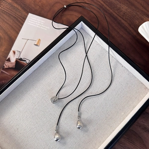 Détail des pendentifs boule et feuille argentés sur un collier en cordon ciré noir