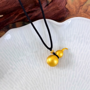 Close-up of matte gold gourd pendant with black woven rope on elegant zen background