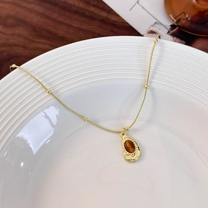 Macro detail of teardrop tiger eye stone pendant on a textured gold necklace chain