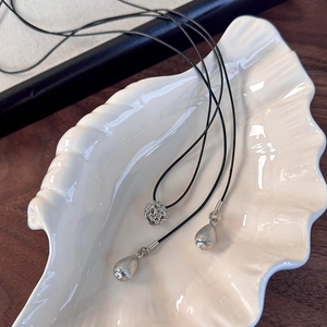 Vue détaillée du collier avec pendentif boule évidée et gouttes d'eau sur un plat coquille