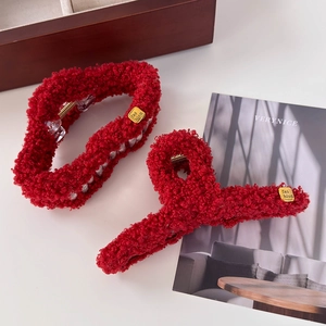 Pinces à cheveux en peluche rouge avec étiquette dorée sur surface blanche et décor