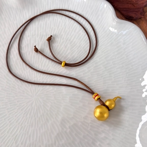 Macro detail of golden sand gourd pendant with brown woven cord on white ceramic