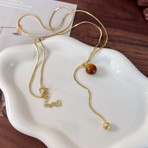 Detail of tiger eye stone pendant on golden snake chain over white ceramic tray