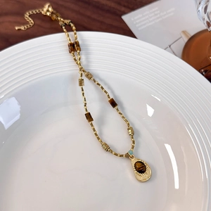 Detail of tiger eye stone pendant and vintage gold beaded chain on ceramic plate