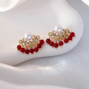 Macro detail of red bead tassel earrings with pearls and crystals on a white pedestal