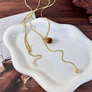 Detail of gold snake chain with brown tiger eye bead pendant and adjustable clasp