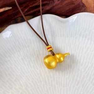 Macro detail of a matte gold gourd pendant with red enamel bead on a brown cord