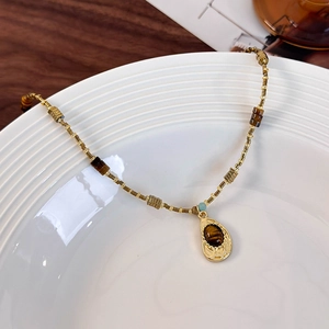 Detailed close-up of tiger eye stone pendant and gold beaded chain on white ceramic plate