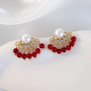 Detailed close-up of gold pearl earrings with red bead tassels and sparkling rhinestones