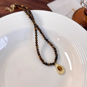 Detail of tiger eye bead necklace with golden teardrop pendant on a white tray