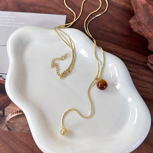 Detail of gold snake chain necklace with brown tiger eye bead in a luxury setting
