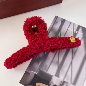 Détail de la pince à cheveux en peluche rouge avec une étiquette métallique dorée fashion