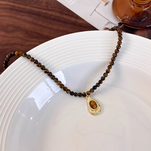 Macro detail of natural tiger eye beaded necklace with gold water drop pendant in ceramic tray