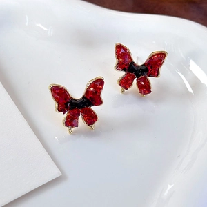 Vintage butterfly earrings with red crystals and black bow details in a white ceramic dish